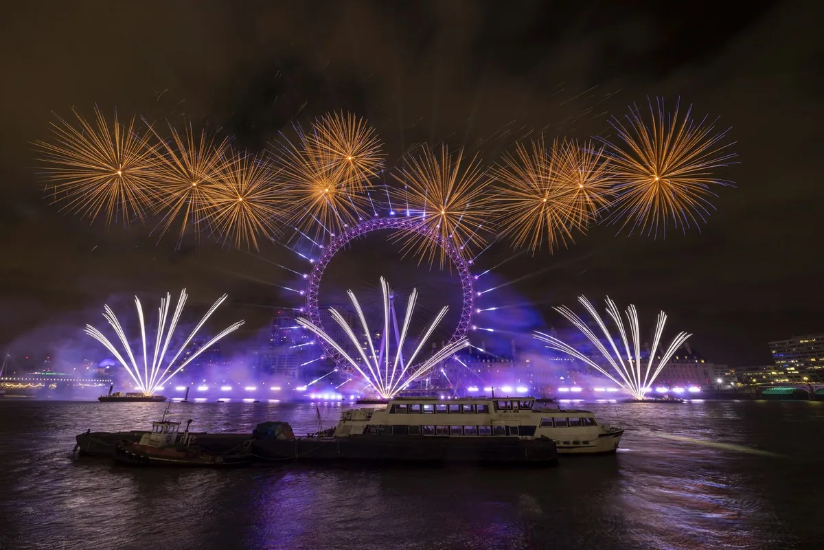 Fireworks bursting on both sides of the London Eye above the Thames at New Year