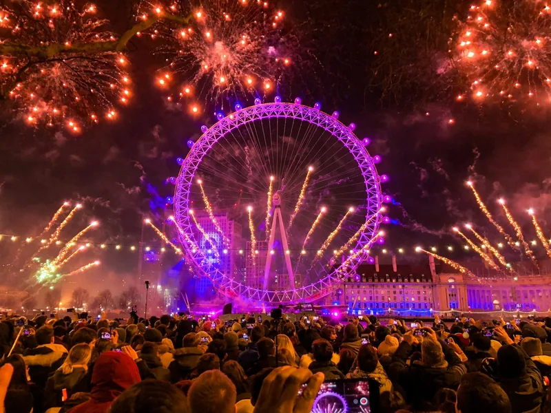 Crowds on the riverside watching New Year fireworks around the pink-lit London Eye