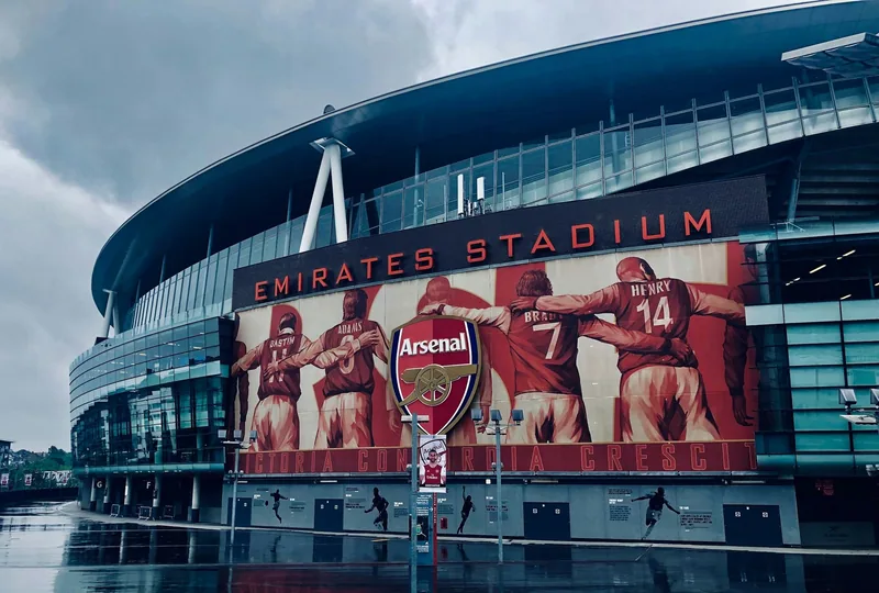 The curved facade of the Emirates Stadium, wrapped in a large mural of Arsenal players