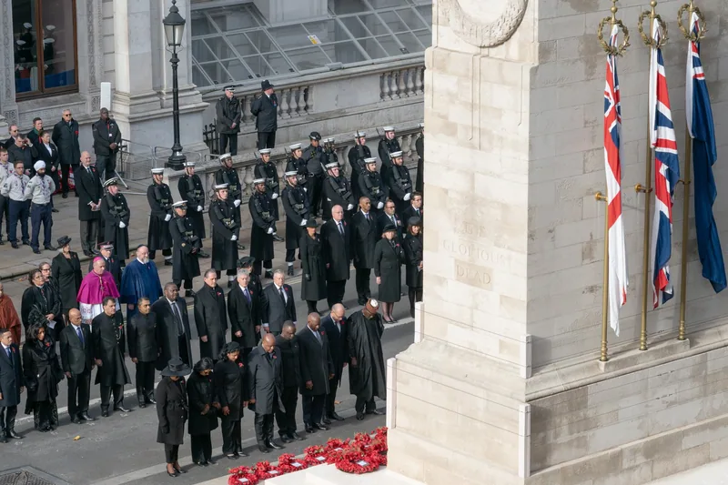 Ranks of people standing in silence beside the Cenotaph on Remembrance Sunday, poppy wreaths at its foot
