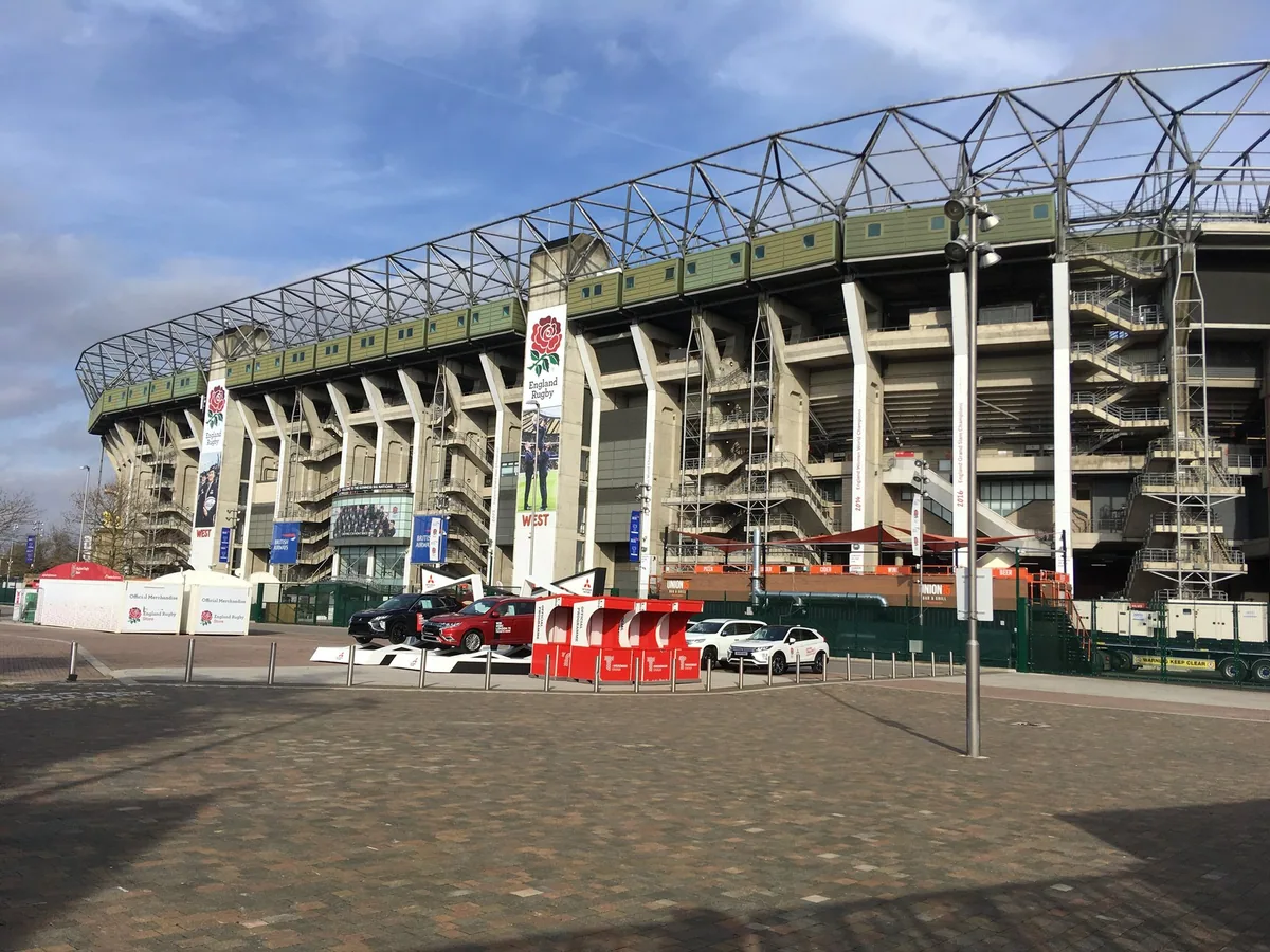 The stands and steel roof trusses of Twickenham Stadium seen from the forecourt on a bright day