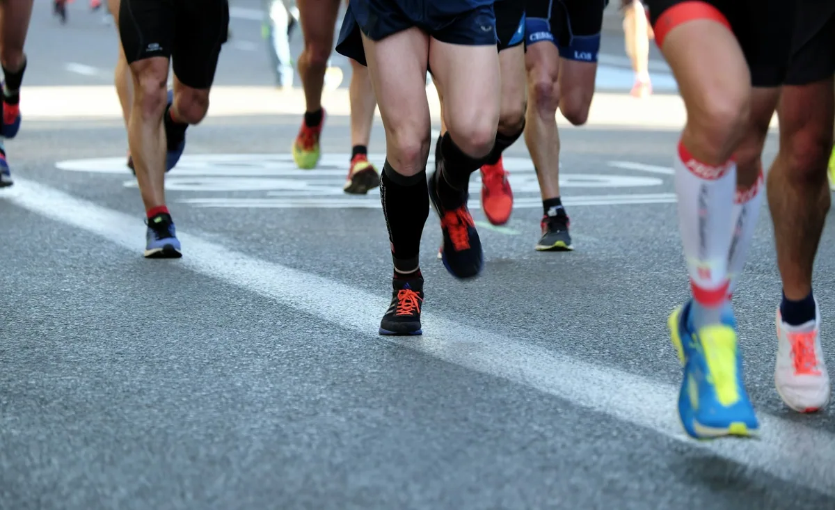 Close view of a group of road runners from the waist down, bright trainers and compression socks striding across a white road marking