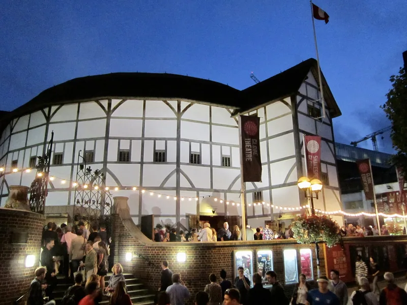 Audiences gathering on the steps outside Shakespeare's Globe at dusk under strings of lights