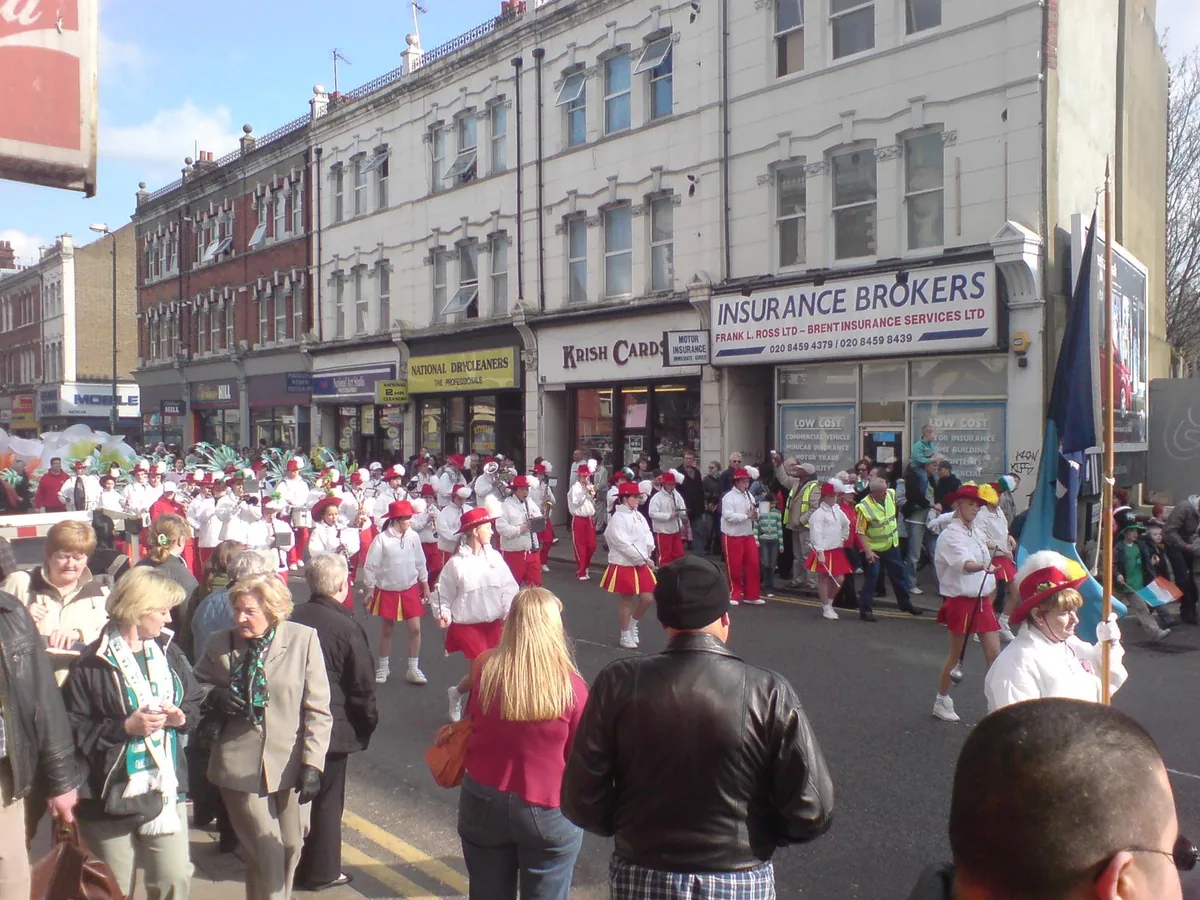 Marchers in white and red filling the road past shopfronts in Willesden Green on St Patrick's Day