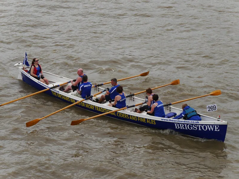 A crew rowing a traditional wooden gig on the Thames, oars out, in the Great River Race