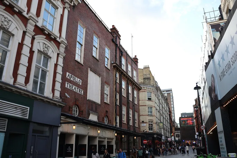 The brick flank of the Apollo Theatre on Shaftesbury Avenue, with show posters and pedestrians below