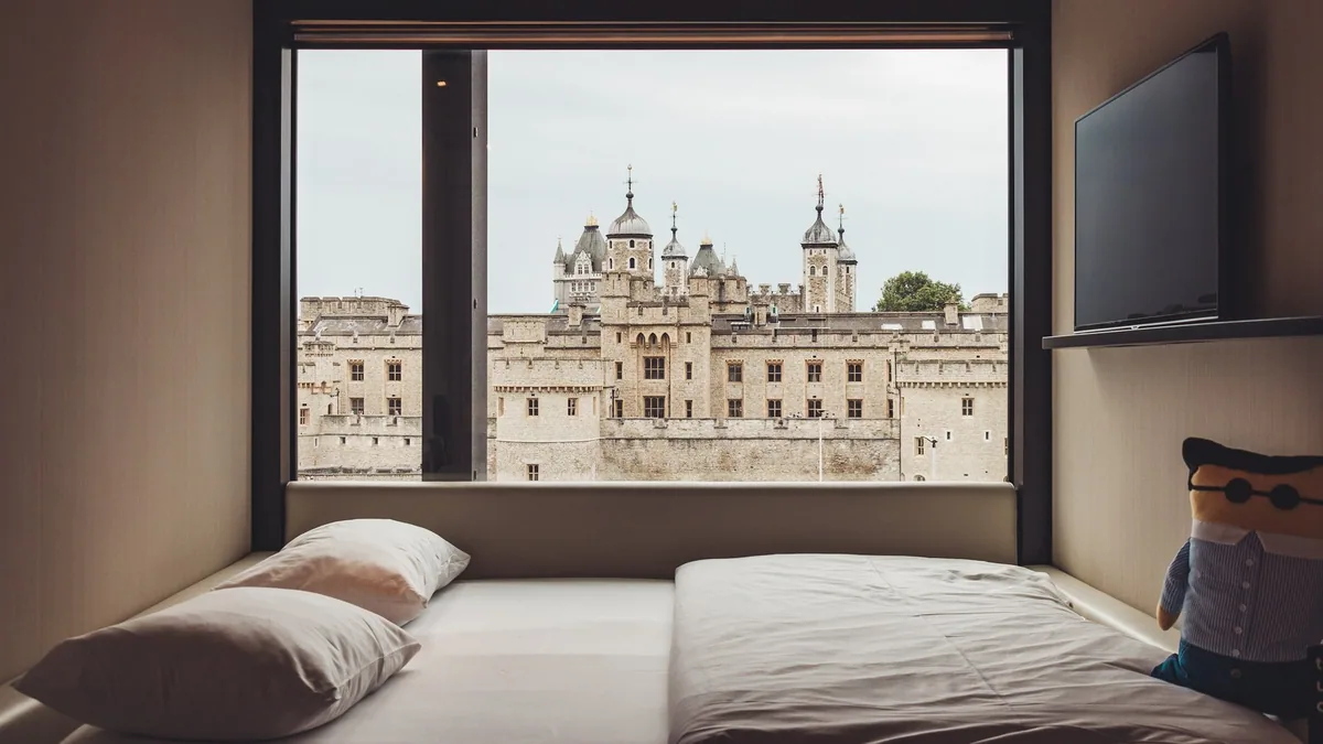 A hotel room bed facing a large window with a view of the Tower of London