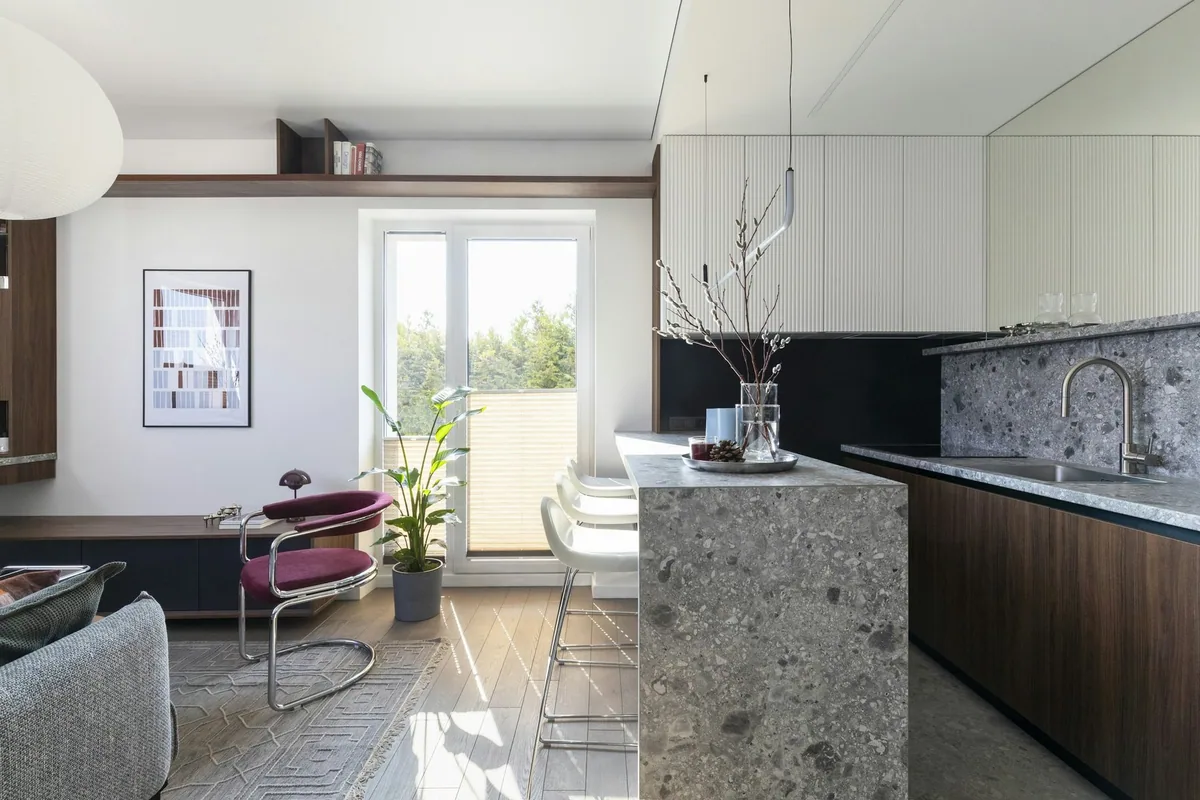 Open-plan studio flat with a stone kitchen island, dining chairs and a living area by the window