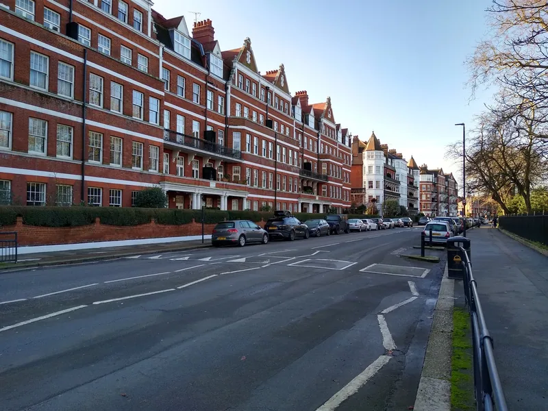 A street of red-brick Victorian mansion flats in London with cars parked along the kerb