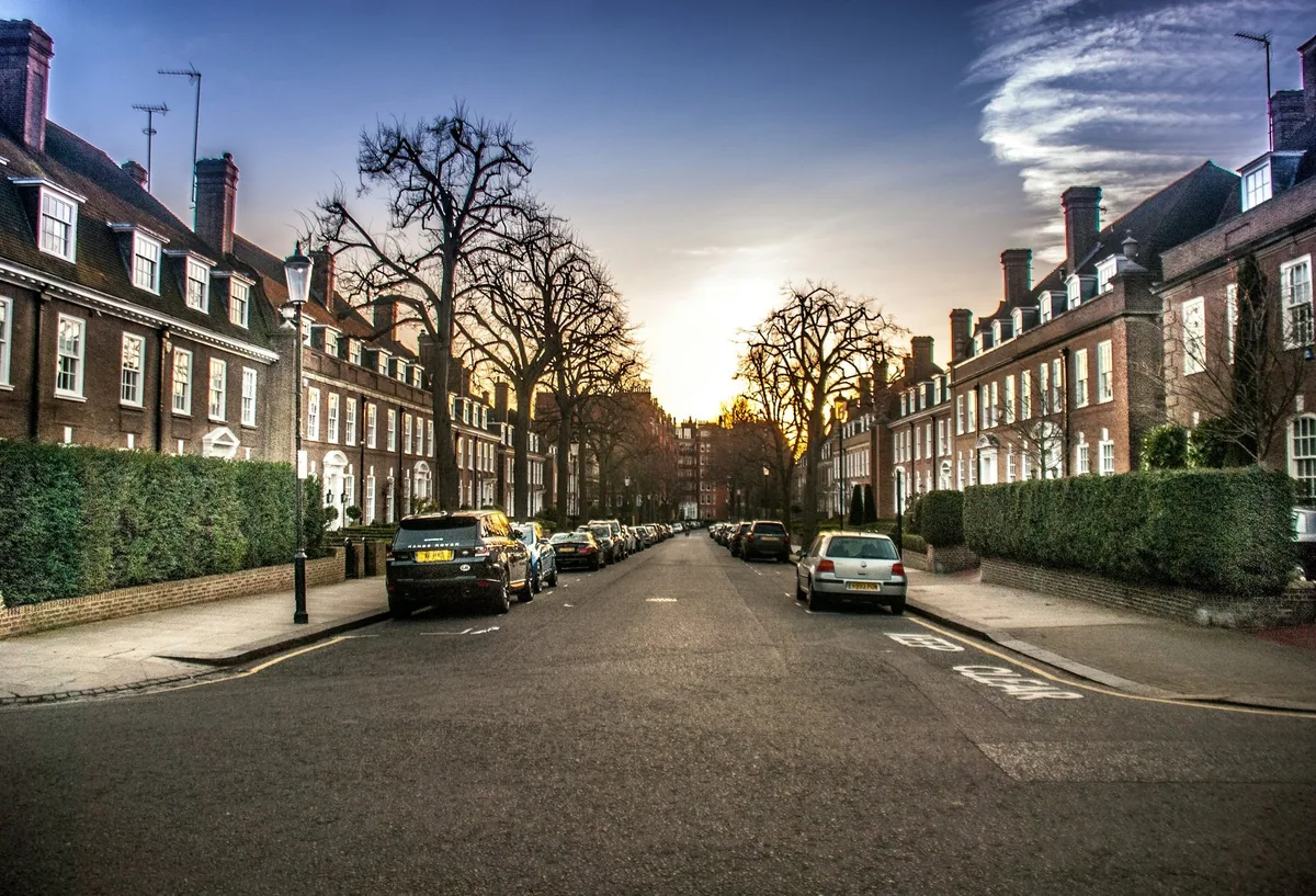 A quiet Kensington street of brick terraced houses with parked cars at sunset