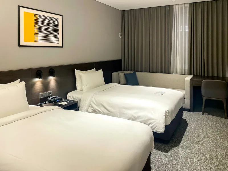 A plain twin hotel room with two beds, a desk and a curtained window