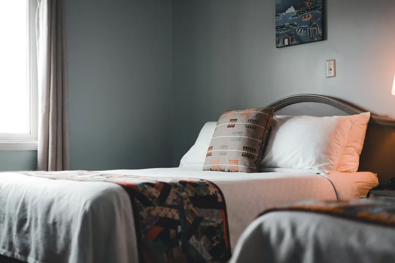 Twin beds made up in a small hotel room with a window and quilted throws