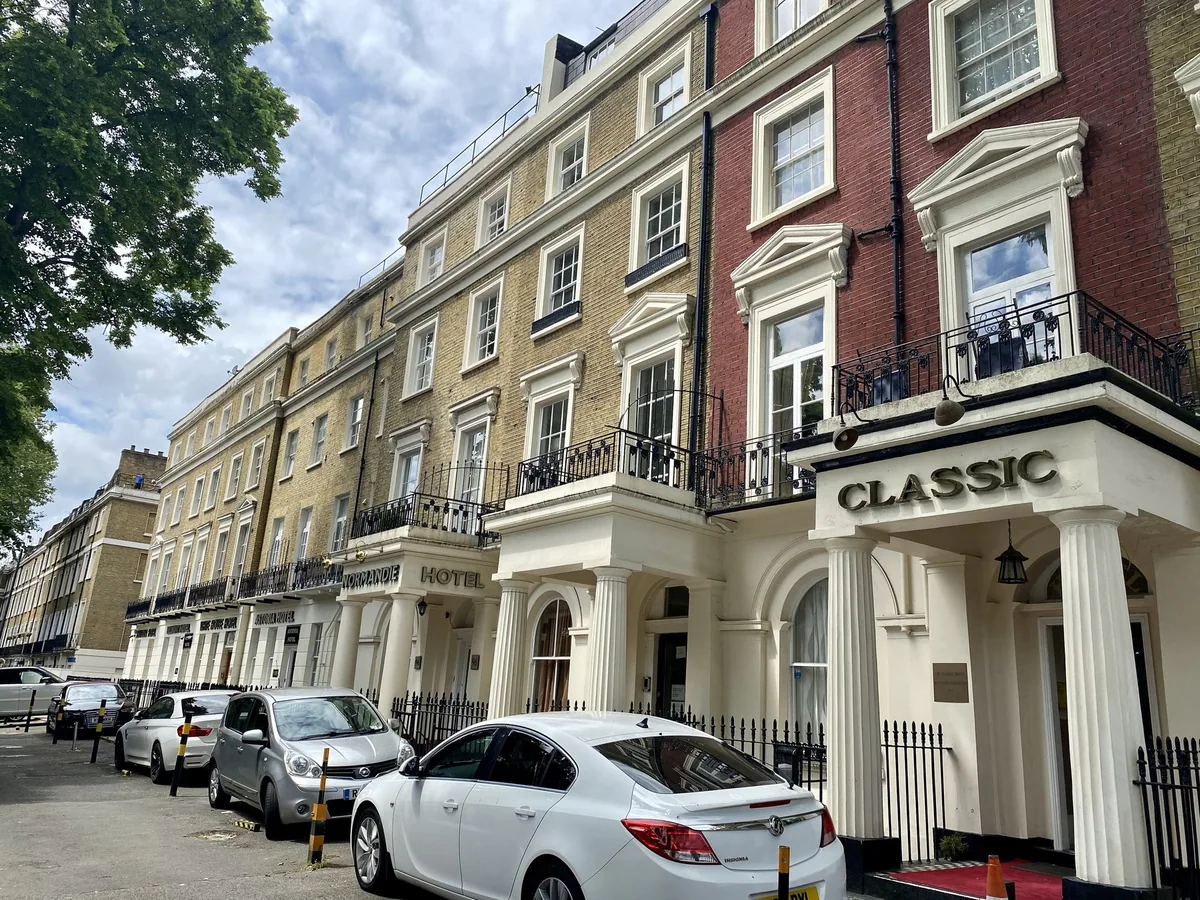 Cars parked in front of a stucco terrace of small hotels on a Paddington street