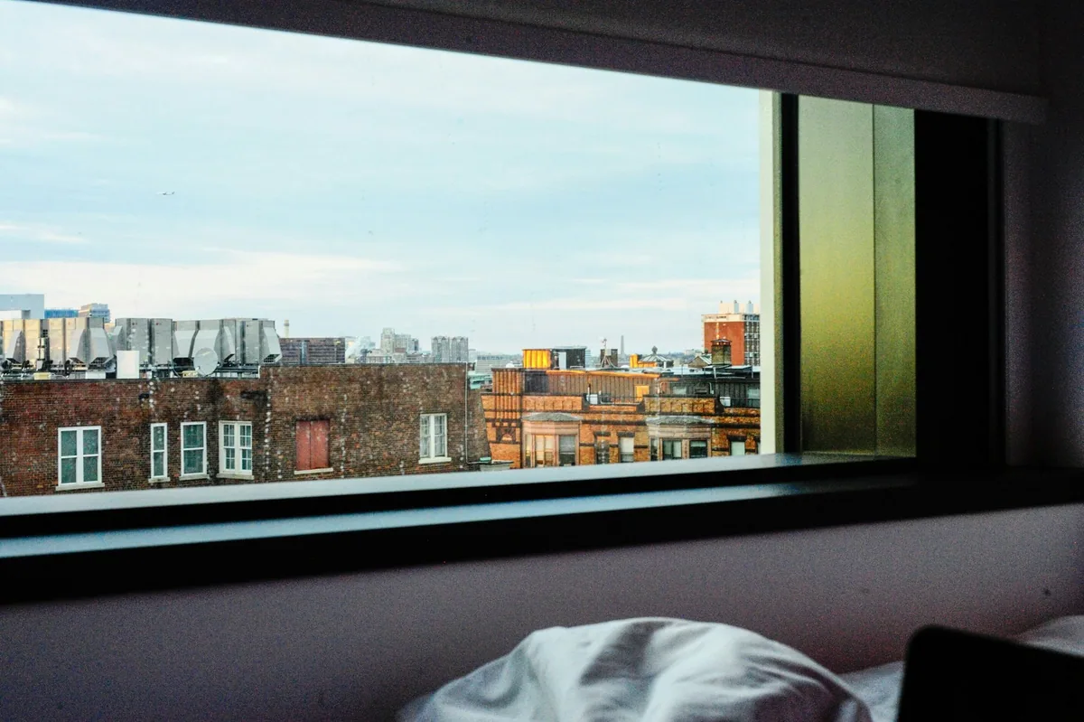A sealed hotel bedroom window looking out over brick rooftops and rooftop ventilation plant