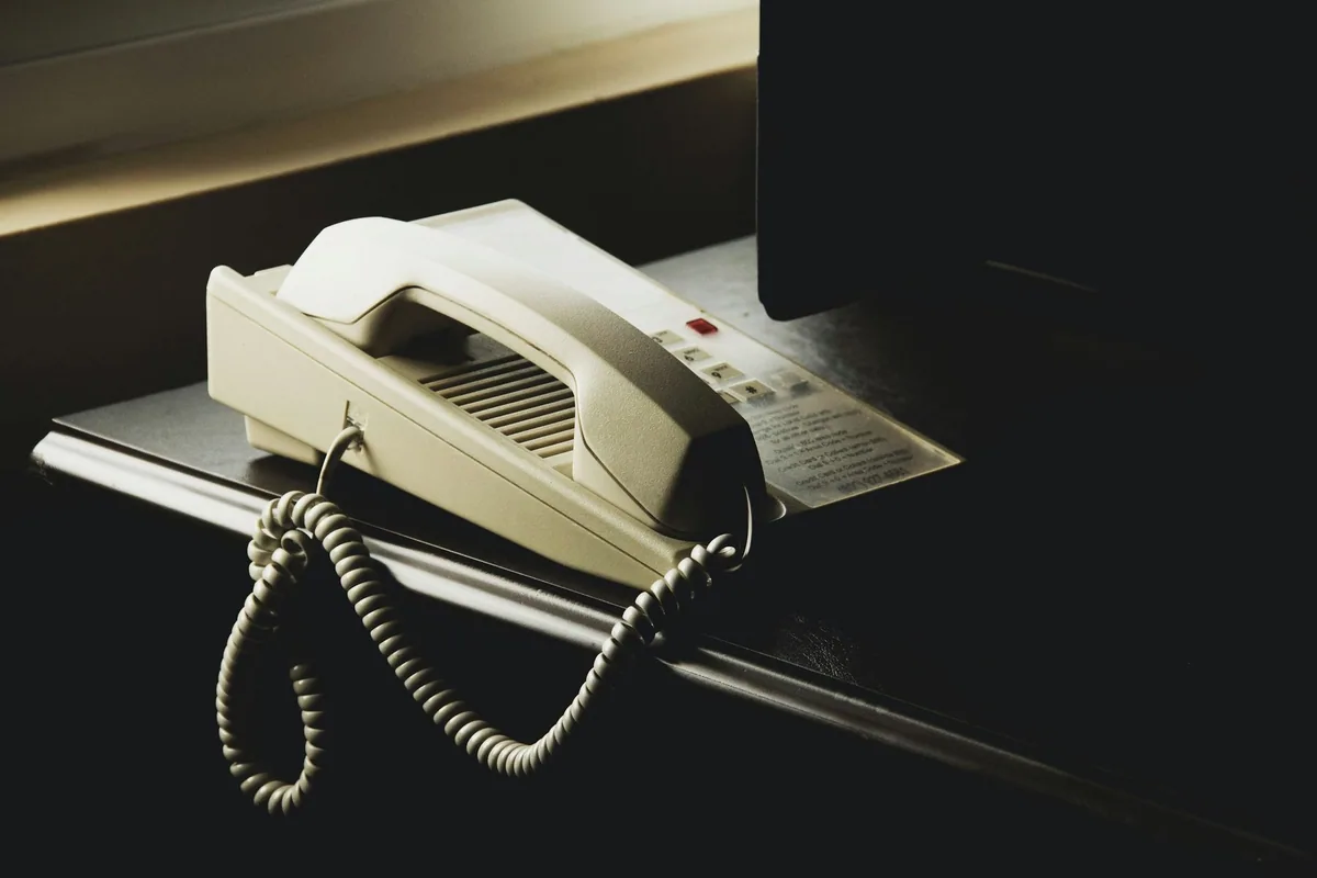An old cream desk telephone on a hotel bedside shelf, with the dialling card beside it