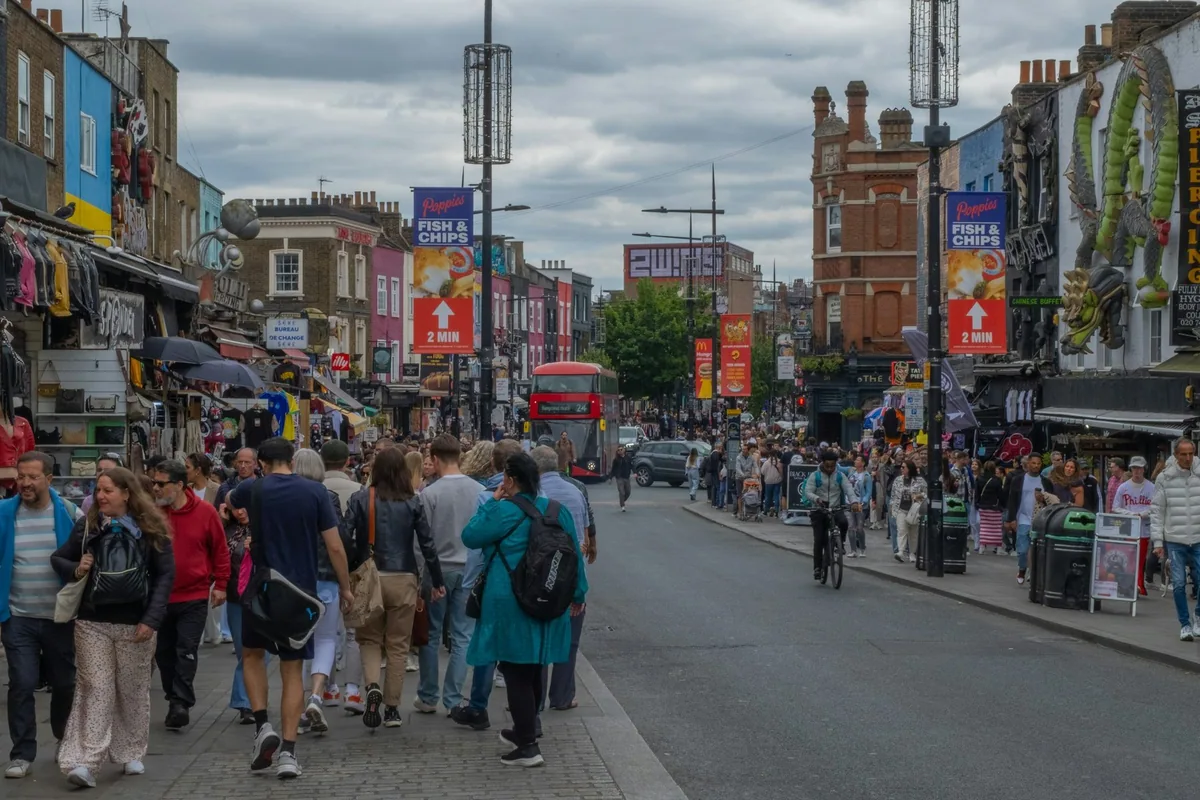 Crowds and colourful shopfronts on Camden High Street with a red bus in the distance