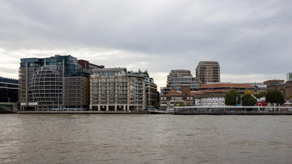 The Bankside riverfront seen across the Thames: flats and offices along the walkway, with the white timbered Globe theatre to the right