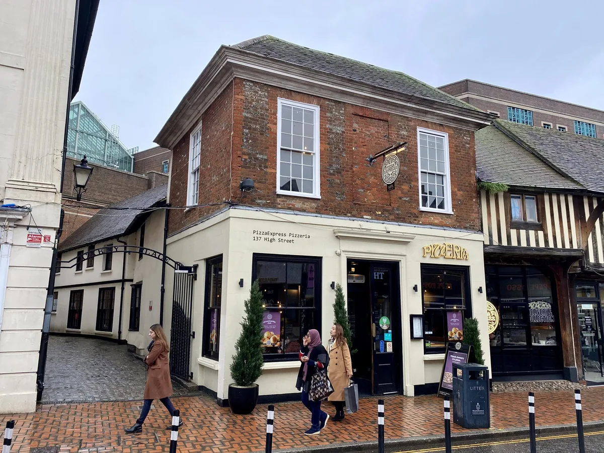 A brick and timber-framed building among shops on the pedestrianised high street in Watford