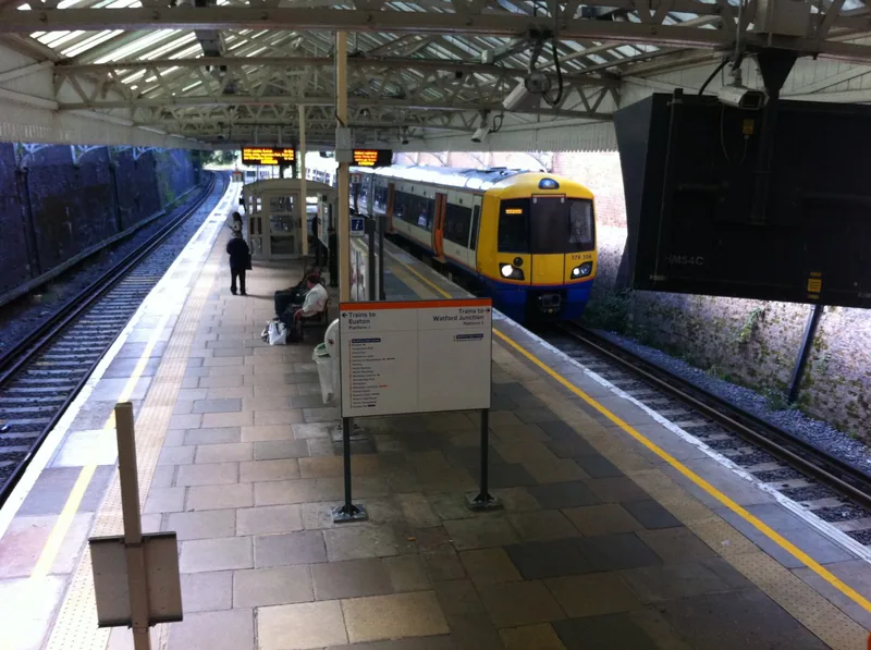 A London Overground train arriving at Watford High Street station with passengers waiting